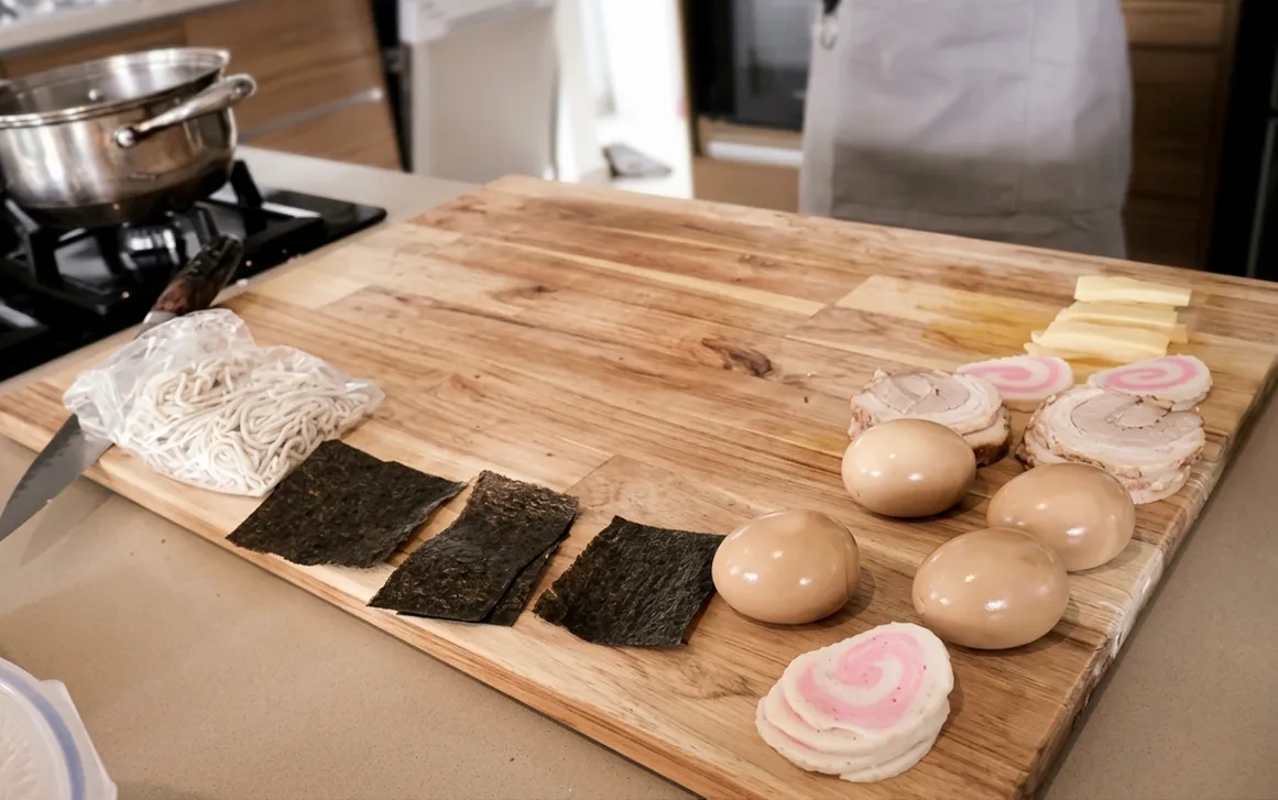 Ingredientes del ramen listos sobre la tabla: fideos, nori, huevos, chashu y narutomaki